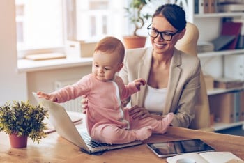 Child care provider letting a baby sit on desk and play with laptop computer.