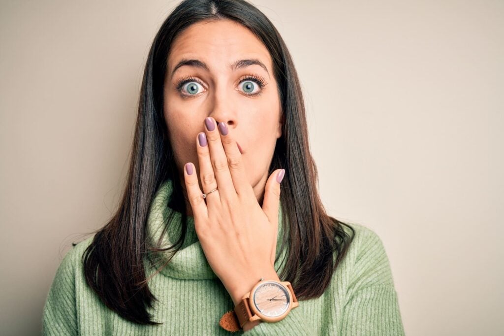 Young brunette woman with blue eyes wearing turtleneck sweater over white background cover mouth with hand shocked with shame for mistake, expression of fear, scared in silence, secret concept