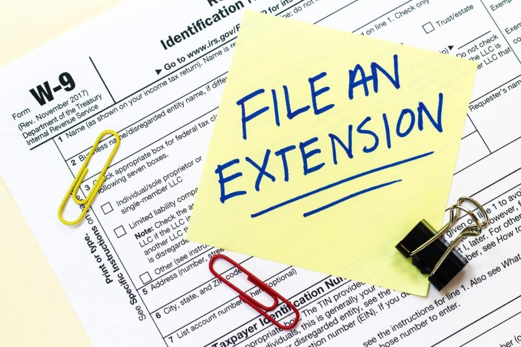 A W9 tax form with File an Extension written on a yellow sticky note.