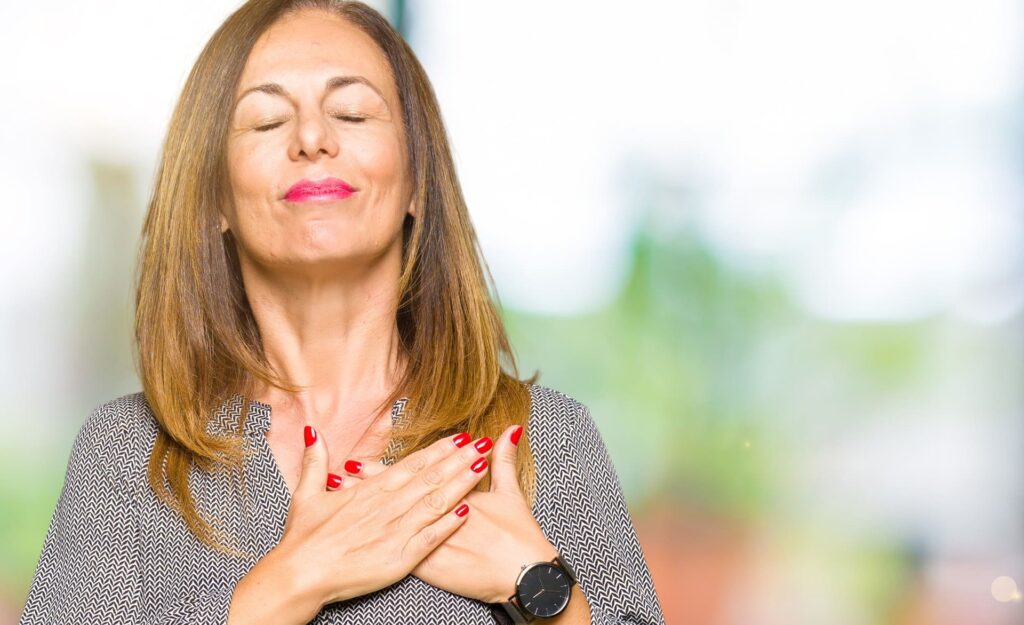 Beautiful middle age business woman smiling with hands on chest with closed eyes and grateful gesture on face. Health concept.